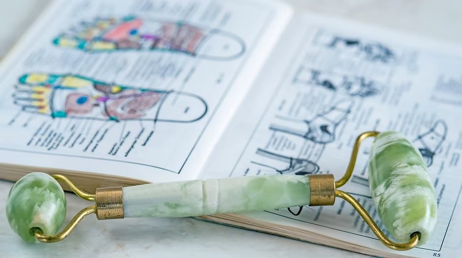 A jade reflexology roller resting on an open reflexology chart book